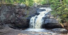 there is a waterfall in the middle of this rocky area with trees on both sides