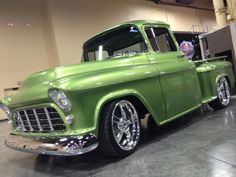 an old green truck is parked in a garage with chrome rims and flat tires