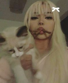 a woman with long blonde hair holding a cat in front of her face and nose