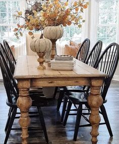 a wooden table topped with black chairs next to a vase filled with flowers and pumpkins