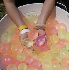 two people are holding hands in a bucket filled with balloons and confetti balls