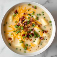 a white bowl filled with potato soup topped with cheese and green onions on a marble surface