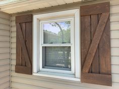 an open window with wooden shutters on the side of a white house in front of a tree