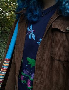 a woman with blue hair wearing a brown corded jacket and dragon t - shirt