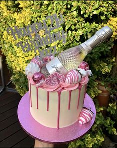 a pink and white cake sitting on top of a table next to a green bush