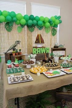 a table topped with green and white desserts next to a window covered in balloons