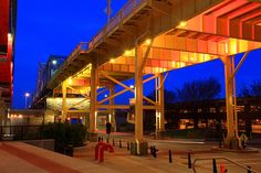 an empty parking lot at night with lights on the walkway and cars parked under it