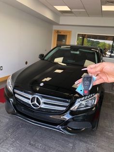 a person holding a remote control in front of a mercedes benz c - class car