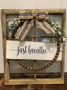 a sign that says just breathe hanging from a window with a wreath around it and greenery