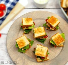 small sandwiches are arranged on a plate with lettuce and tomatoes in the background