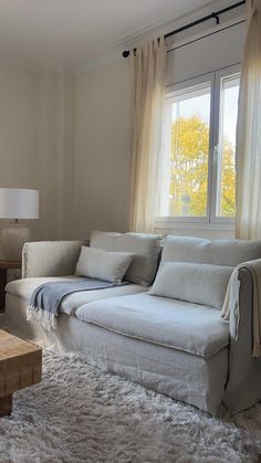 a living room filled with furniture and a large window next to a white rug on top of a hard wood floor