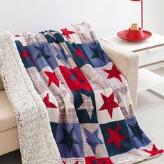 a red, white and blue quilt on a couch in a living room next to a lamp