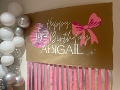 a birthday sign with balloons and streamers on the wall next to it is a pink and silver comb