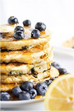 stack of pancakes with blueberries and syrup on white plate next to lemon wedges