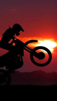 a person on a dirt bike doing a trick in the air with the sun setting behind them