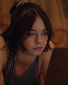 a young woman sitting on top of a bed looking at a laptop computer screen in front of her