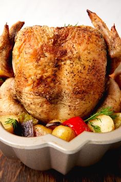 a roasted chicken in a roasting pan with vegetables