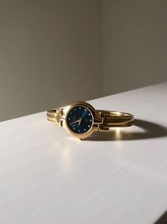 A gorgeous blue color dial and gold-plated watch bangle from 90s Givenchy. Instead of numbers, this watch is studded with rhinestones. Rank Condition B Good Condition with signs of wear -Minor inconspicuous scratches -Deep dents (few) on the bangle -Watch is functional (Battery changed last August 2024) Color: Blue Dial, Gold Bangle Material: Stainless Steel, Gold-plated Closure: Jewelry Clasp Mechanism: Quartz, Battery-operated Antique Gold Watches With Subdials, Antique Gold Watches With Polished Finish, Elegant Blue Watch With Metal Dial, Vintage Blue Watch With Subdials, Vintage Blue Watch With Tachymeter, Gold Plated Watch, Simple Packaging, Bangle Watches, Jewelry Clasps