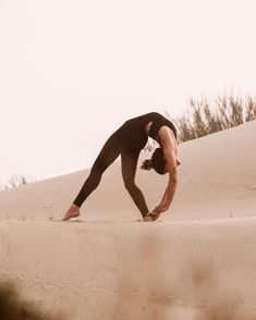 a person doing a handstand on top of a sand dune in the desert