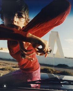 a woman in red shirt sitting on the back of a car holding onto an object