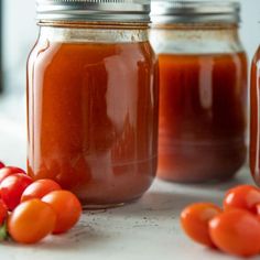 three jars filled with tomato sauce and some tomatoes on the table next to them,