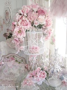 a white birdcage filled with pink flowers on top of a table