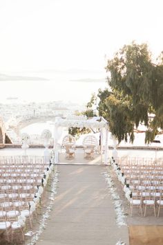 an outdoor ceremony setup with white chairs and greenery on the aisle, overlooking the water