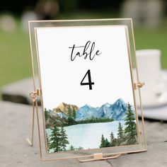 a table number with a mountain lake in the background and a cup of coffee to the side