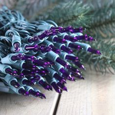 a bunch of purple and silver christmas lights sitting on top of a wooden table next to evergreen branches