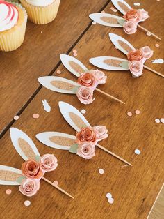 some cupcakes are sitting on top of the table with paper flowers and bunny ears