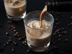 coffee being poured into two glasses filled with ice and coffee beans on a black surface