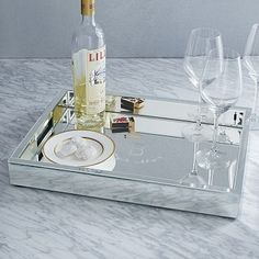 a glass tray with some wine glasses and bottles on it, sitting on a marble table