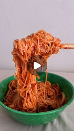 someone is eating noodles with chopsticks in a green bowl