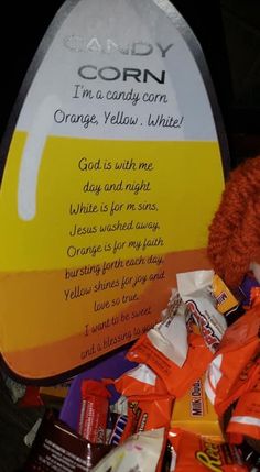 an orange teddy bear sitting next to a sign with candy on it's side