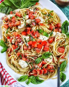 pasta with tomatoes, basil and mozzarella on a white plate next to silverware