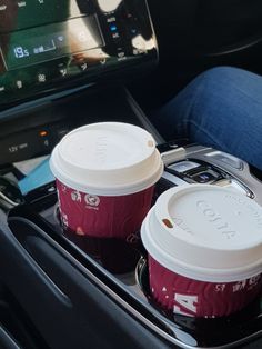 two coffee cups sitting in the center console of a car