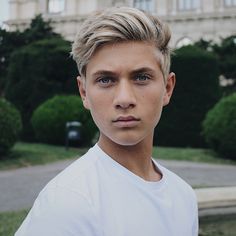 a young man with blonde hair and blue eyes posing for a photo in front of a building