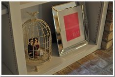 a birdcage with two dolls in it sitting on a shelf next to a framed photo