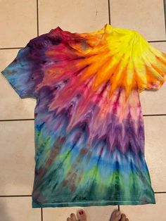 someone is holding up a tie - dyed t - shirt in front of their feet