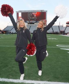 two cheerleaders pose on the football field with pom poms in their hands