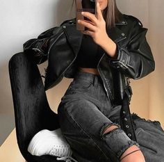 a woman in black jacket and ripped jeans taking a selfie with her cell phone