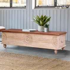 a wooden bench sitting on top of a rug next to a plant in a pot