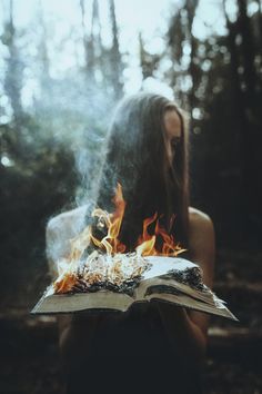 a woman sitting in the woods reading a book with fire coming out of her face