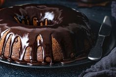 a bundt cake with chocolate icing on a black plate next to a knife