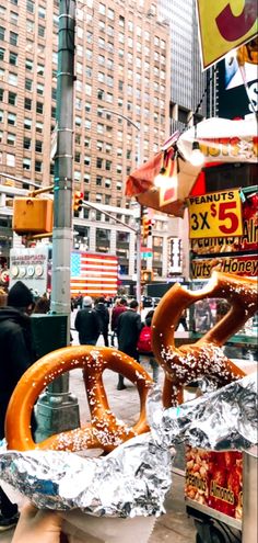 two giant pretzels wrapped in tin foil on a street corner with people walking by