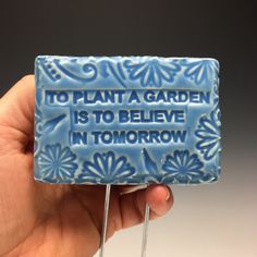 a hand holding a blue and white lollipop that says to plant a garden is to believe in tomorrow