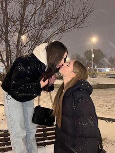 two women kissing each other on a bench in front of snow covered park benches at night