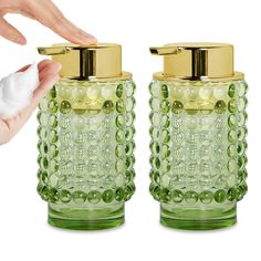 two green glass bottles with gold lids and one is holding something in it's hand