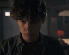 a young man in a black shirt stares at the camera while standing in a dark room