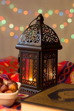 a small lantern sitting on top of a table next to a bowl of fruit and a book